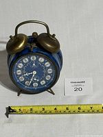 Front angle view of the antique Wehrle alarm clock showing blue body, twin brass bells, and Roman numeral clock face with two smaller dials