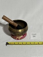 Tibetan singing bowl resting on fabric cushion with wooden mallet inside, measuring approximately 4 inches in diameter.