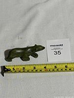 Side view of dark green jade carved walking bear with tape measure showing approx. 4 inch length.