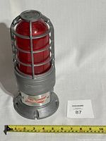 Full view of Budweiser branded red hockey goal light with protective metal cage and red dome lens against white background, tape measure shows 10 inches approximately.