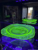 Plate under UV light showing bright green glow confirming uranium glass material with parrot and floral border pattern.