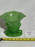 Front angled view of green pressed glass vase showing two nude ladies sculpted on the side, flared opening, geometric base, 8 inches wide