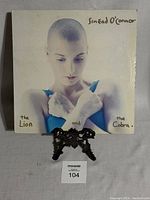 Front cover of the 1987 Sinead O'Connor The Lion and the Cobra LP vinyl record showing a portrait of Sinead O'Connor with a shaved head and arms crossed, title text in black on simple cream background.