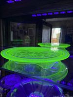 Green uranium glass cake plate glowing bright green under UV light, showing detailed Princess pattern and footed base.