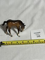 Ceramic horse foal figurine positioned next to tape measure for size reference, showing length around 4 inches.