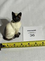 Side angle of vintage ceramic Siamese cat figurine with measuring tape to show size around 4.5 inches tall.