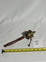 Full view of the prayer wheel lying horizontally next to a measuring tape showing a length around 19 cm.