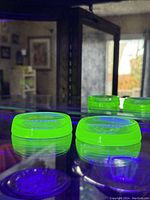 Two green Vaseline Uranium Glass coasters glowing under UV light on glass shelf.