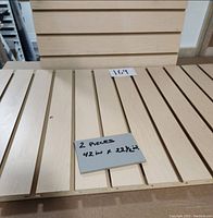 Two light-colored melamine slatwall panels placed flat, showing horizontal grooves spaced evenly across the width. A note card reads dimensions 42 inches by 22.5 inches.