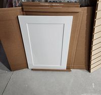 Three white flat panel cabinet doors leaning against cardboard boxes on floor.