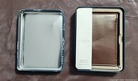 Open blue metal tin box containing brown Fossil leather wallet with white band label inside.