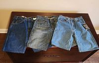 Three pairs of jean shorts laid flat on a dark wooden surface showing front view.