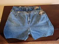 Two pairs of light and medium wash jean shorts laid flat on furniture, tags visible showing size 42 waist and brand Five Jungle Co.