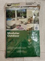 Photo of new Modular Outdoor Protective Cover in original packaging with label indicating size, usage for corner sectional and brand Home Care.