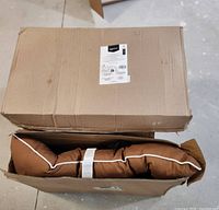 Two large brown dog beds folded inside a box, showing the product packaging.