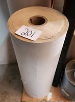 Full side view of the large roll of masking paper standing upright on the floor, showing its height and diameter.