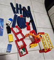 Photo showing various blue plastic track sections, red bridge supports, yellow crane with articulated arm, and small signal light.