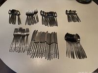 Full display of the flatware set laid out on a table, showing the various types of forks, knives, and spoons, all with matching floral patterned handles.