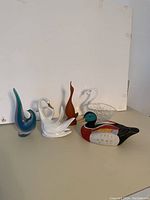 Overview of all five bird figurines including the wooden duck decoy, glass swan bowl, porcelain swans, abstract glass bird, and wooden bird sculpture.