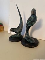 Two bronze bird sculptures with brass beaks, green-black patina, sitting on round wooden bases with visible wear.