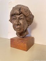 Front view of bronze woman’s head sculpture on a solid wood base showing detailed facial features and hair texture.