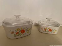 Two Corningware Wildflower pattern casseroles with glass lids side by side showing front floral design and shape.