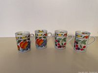 Four porcelain cups with fruit designs arranged side by side, showing the full set.
