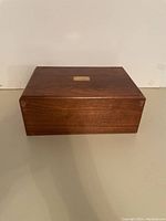 Closed rectangular wood jewelry box with polished finish and gold plate on the top