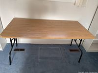 Front view of the large folding table showing wood finish top and black metal legs.