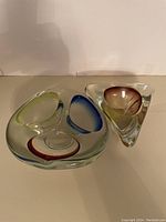 Two Mid-Century Modern style thick glass ashtrays with colorful tinted areas shown from above on neutral surface.