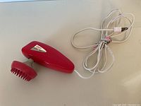 Red Oster infrared massager device with wired power cord shown from side angle.