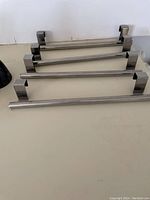 Four stainless steel over cabinet hangers with black coated hooks laid out on a flat surface.