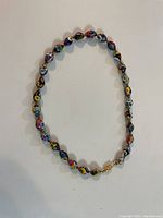 Painted glass bead necklace arranged in a loose oval shape showing colorful, detailed floral patterns on each bead.