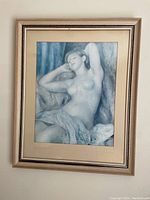 Front view of framed artwork showing nude female figure reclining, print and mat visible under glass, wood frame around.