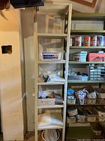 Tall beige metal shelving unit with six shelves, empty except for some packaging on lower shelves, placed against a wall in a garage or workshop environment.