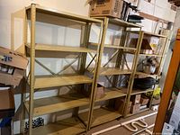 Three metal garage shelving units with five shelves each, set up in a garage space with various items stored on some shelves.