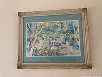 Front view of the framed print showing the garden patio scene with wicker chairs enclosed by a carved wooden frame and glass.
