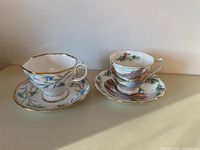 Two floral patterned tea cups with matching saucers on a beige surface against white background.