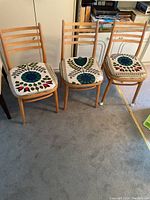Set of three wooden ladder back chairs with floral upholstered seats in a room with carpeted floor, some minor wood scuffs visible.