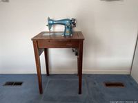 Full view of the vintage Stitchmaster sewing machine mounted on a wooden table, showing the cabinet and legs with the machine on top.