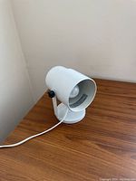 White metal desk lamp on wooden surface, showing front and internal lamp head with bulb