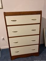 Front view of wooden chest of drawers with four white drawers and metal handles