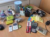 Wide view of lot on wooden desk showing iPods, camera, calculator, Sharpie, watercolor set, assorted stationery and black radio