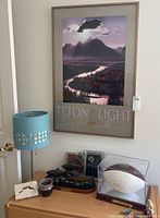 Wide view of framed Teton Light print hanging on wall above dresser with various items including autographed football, lamp, photos, sculpture, and ceramic pot.