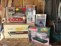 Lot of vintage Coleman camping items and accessories in original boxes shown from front view.