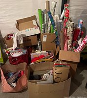 Boxed and bagged lot including multiple rolls of Christmas wrapping paper, gift bags, boxes, and tissue paper seen from front