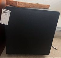 Black DCM VLS-2 loudspeaker subwoofer, side view showing its shape and texture, with a woven basket on top.