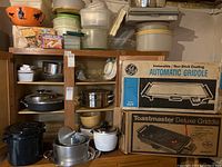 Full shelving unit with assorted food storage containers, mixing bowls, pots, pans, and boxed kitchen appliances including griddles.