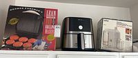 Shelved view of all three items: George Foreman grill in box, Instant Pot air fryer, Braun juice extractor in box