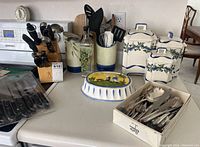 Overview photo of all kitchen items on counter including knife block, ceramic canisters, decorative plate, cutlery set, utensil holders, and oil bottle.